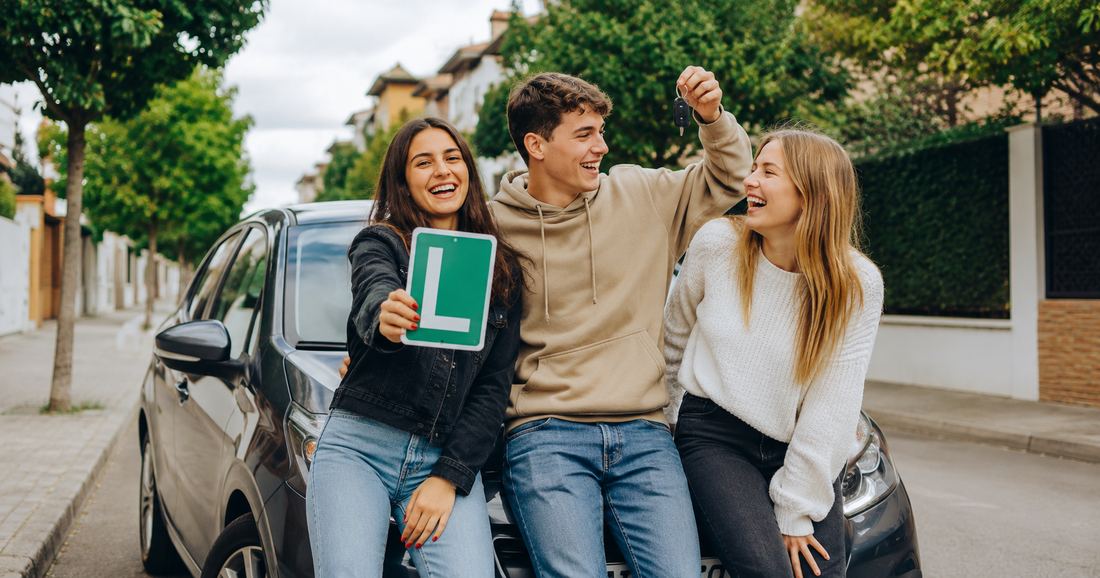 Tres amigos jóvenes celebran junto a un coche: uno enseña la placa L y otro levanta las llaves